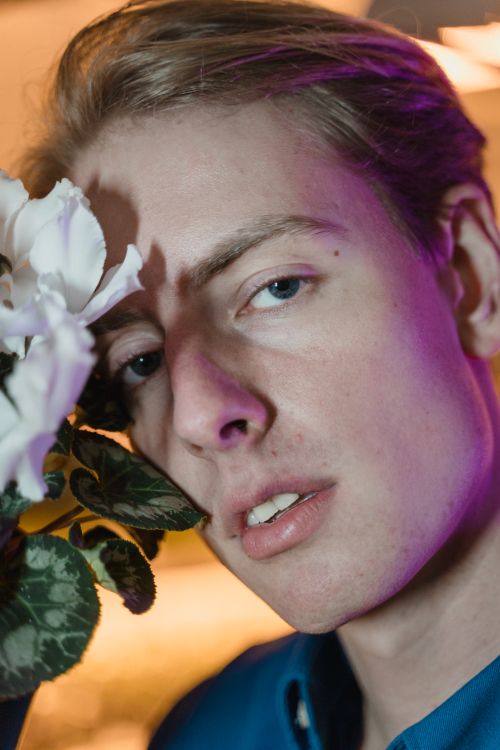 Free A creative close-up portrait of a young man posing with white flowers under colorful lighting. Stock Photo