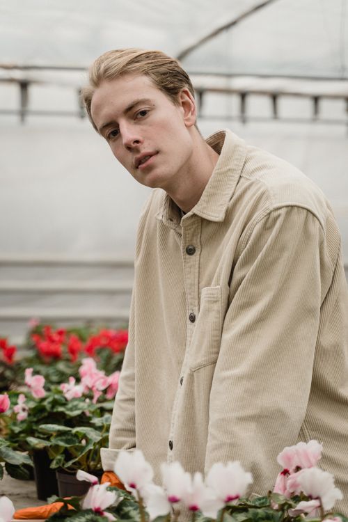Free Portrait of a man in a beige shirt surrounded by vibrant flowers in a greenhouse setting. Stock Photo