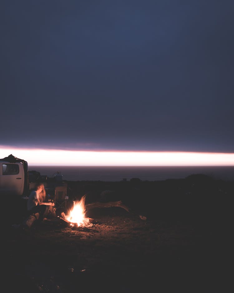 Faceless Person Resting Near Fireplace In Nature At Night