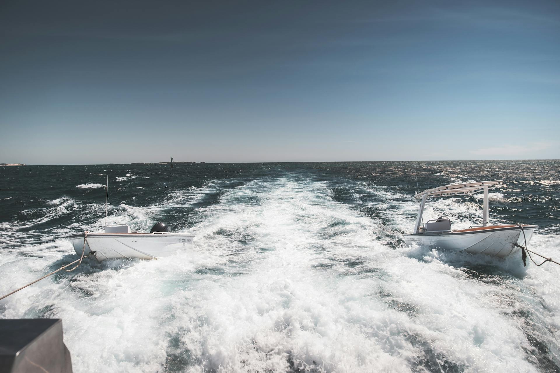 Modern yacht pulling small motorboats on ropes on rippling foamy seawater on clear day