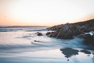 美丽的日落天空下，泡沫波浪般的海水冲刷着粗糙的岩石海岸，风景优美