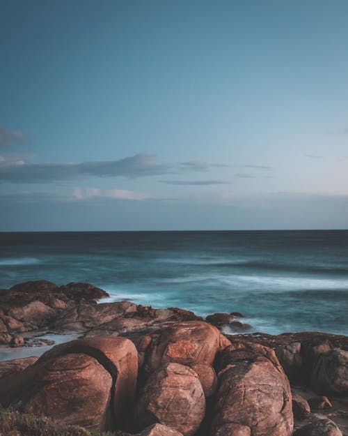 Amazing scenery of rough rocky formations located on coast of turquoise wavy sea against sunset sky