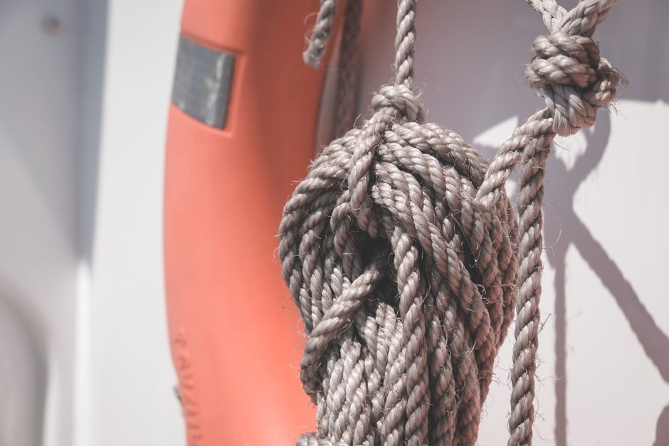 Close-up of a knotted rope and lifebuoy on a boat, capturing the nautical theme in bright sunlight.