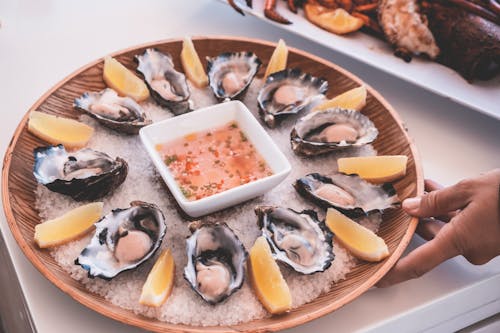 Free Anonymous person serving plate of fresh oysters with sauce and lemons on table Stock Photo