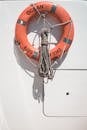 Orange lifebuoy with tied mooring rope hanging on white wall of modern yacht on sunny day