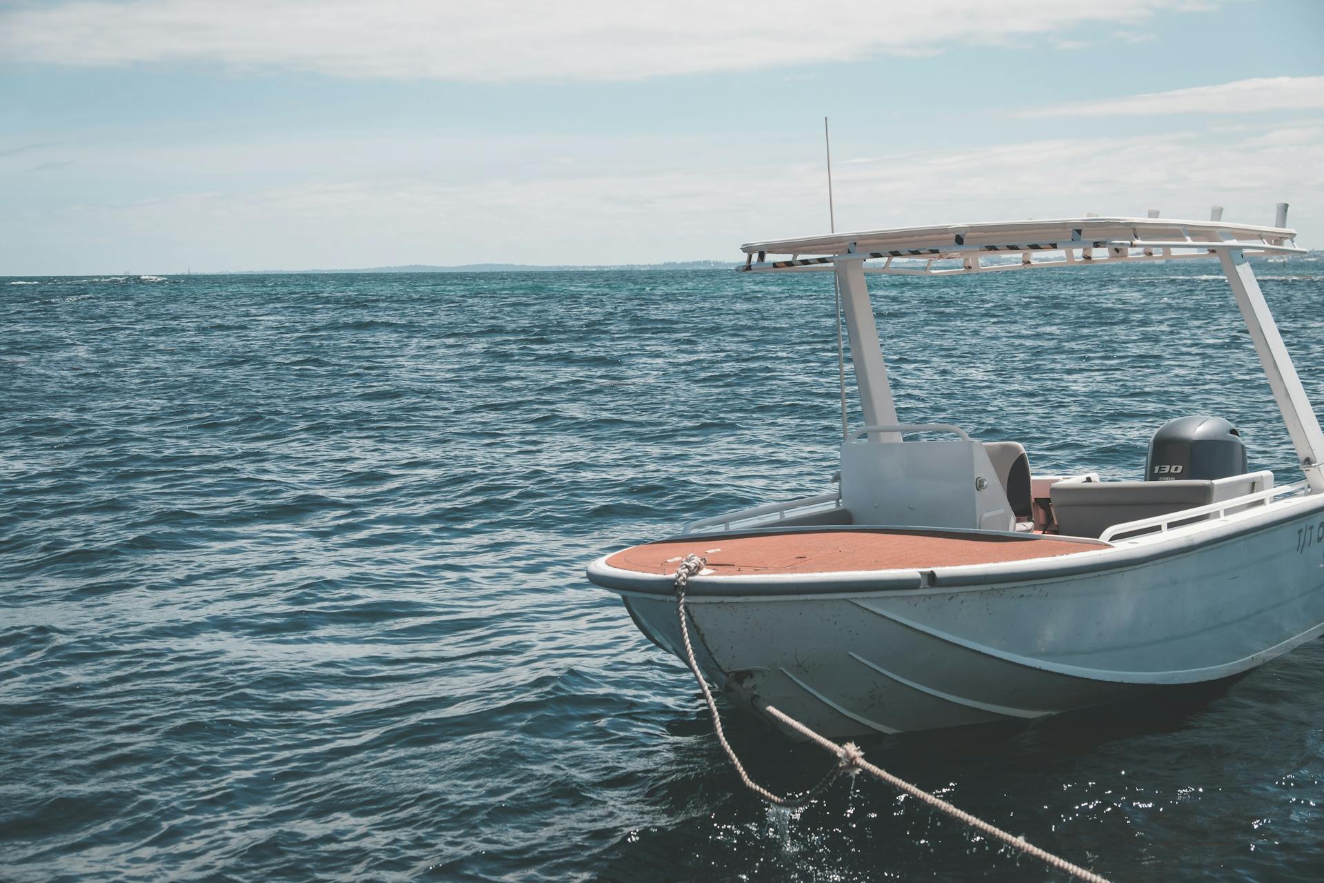 Modern white motorboat with canopy moored on wavy sea near port on sunny day