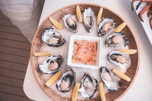 From above of wooden tray with fresh raw oysters served on table with mignonette sauce and lemon slices on chopped ice on yacht