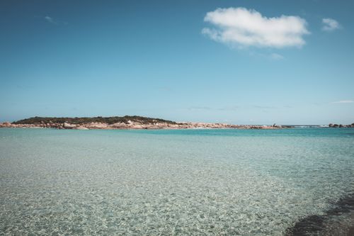 Free Shallow transparent water of still sea against grassy island and blue cloudy sky in tropical resort in sunny summer day Stock Photo