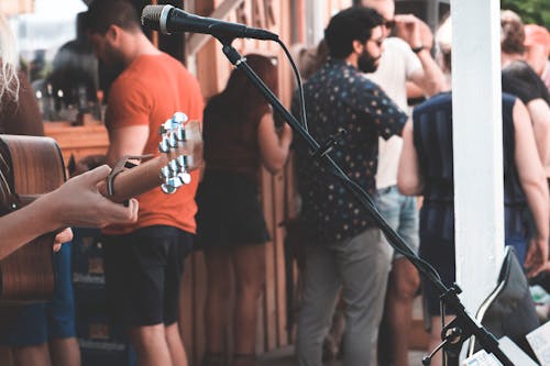 Crop anonymous person with acoustic guitar at festival with many people in daytime