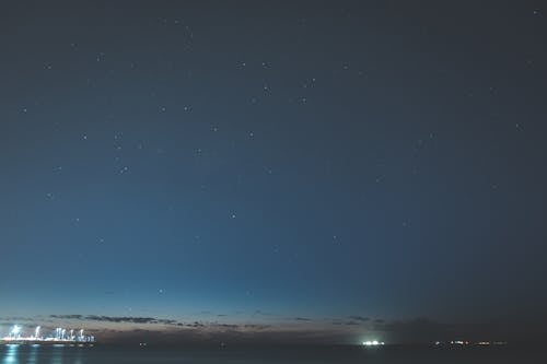 Calm river with luminous lights at port of town under clear dark sky with shimmering stars