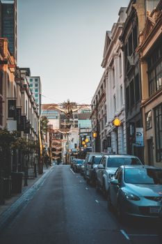 Prestige automobiles on narrow asphalt road surrounded with modern buildings on urban street in daytime