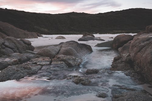 Foamy water of river washing huge rocks of stony coastline under cloudy sky