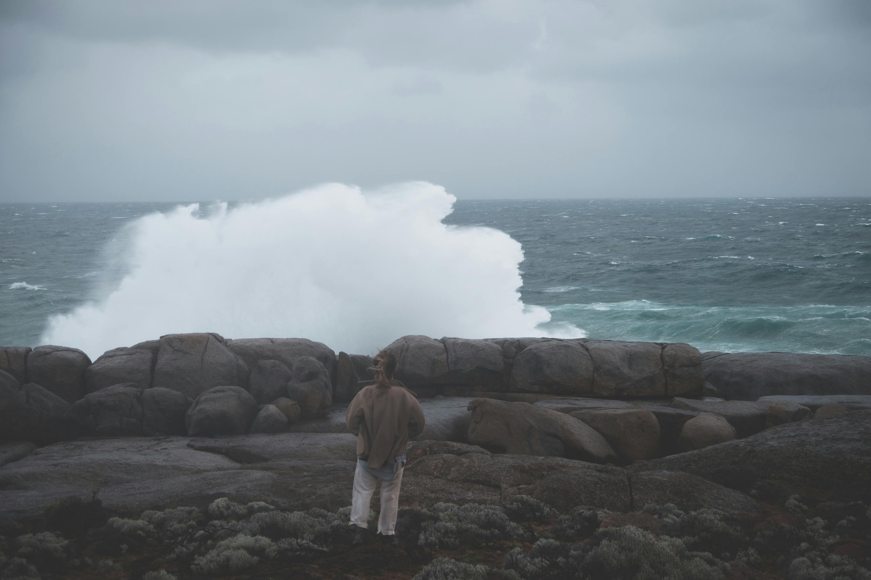 person standing on rocky coast and looking at stormy sea