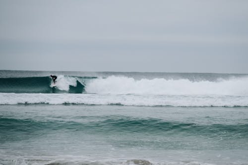 Anonymous surfer riding surfboard on foamy waves of powerful stormy sea in cloudy day