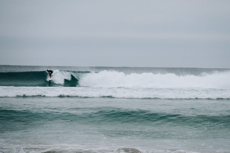 Surfer Riding On Waves Of Ocean In Cloudy Day