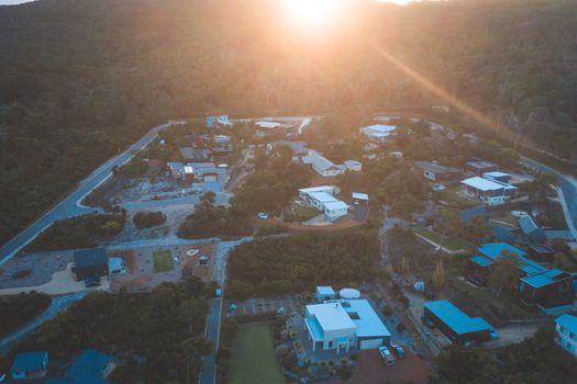 Aerial view of small town placed among green plants illuminated by bright sunlight in daytime