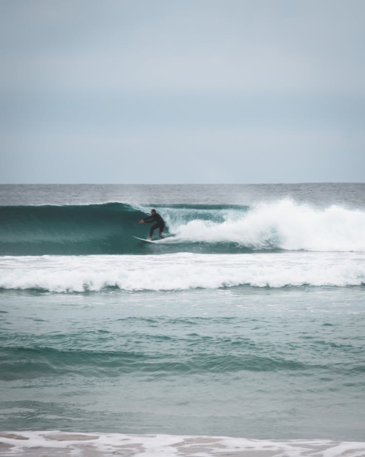 Unrecognizable Surfer Riding On Wavy Sea In Daylight