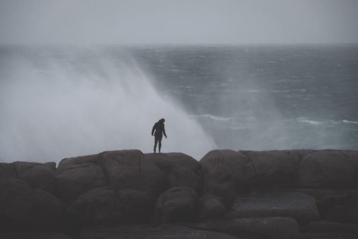 Figure standing on rocks as surf breaks behind — photo by Lachlan Ross on Pexels