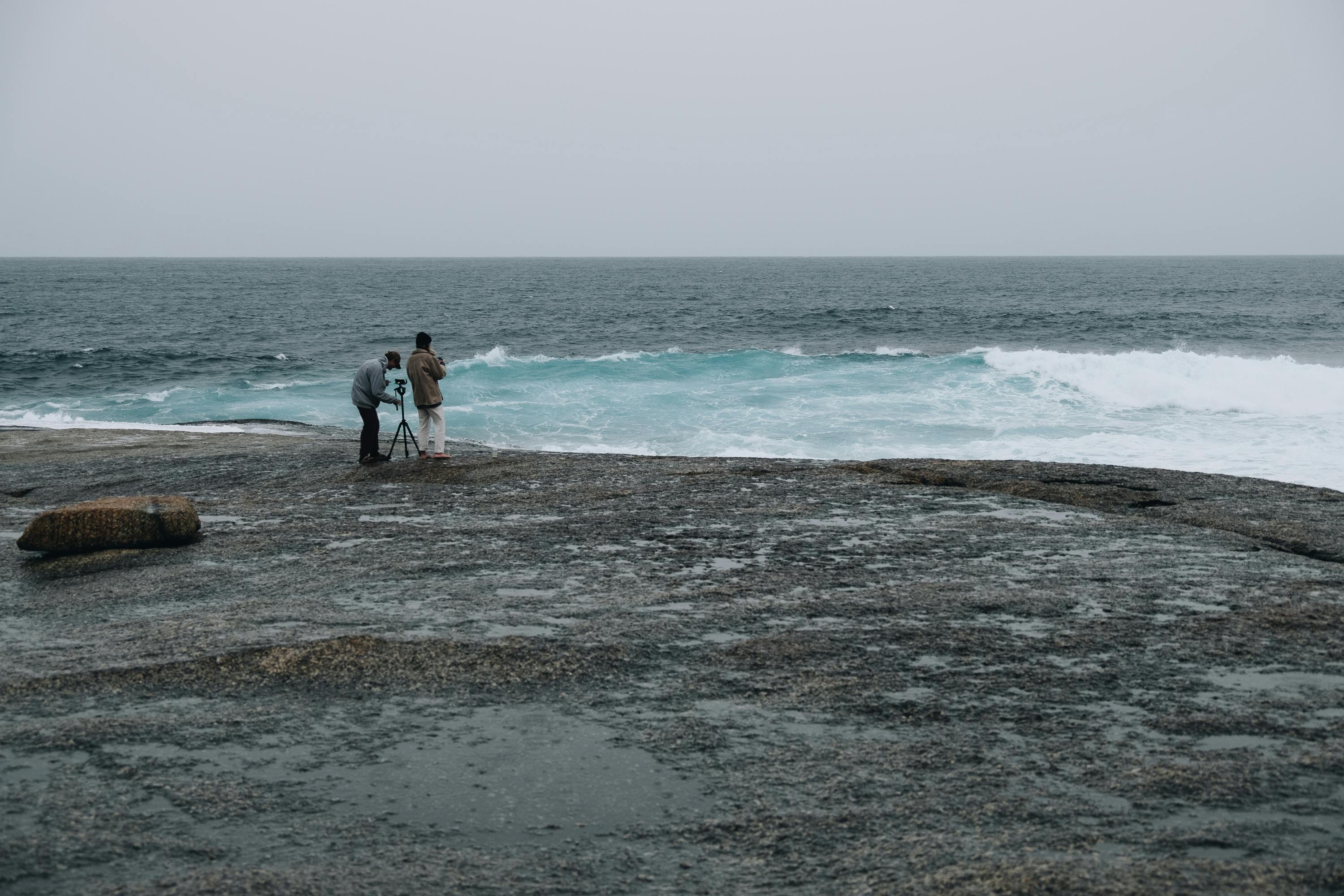 photographers standing on shore and taking photos of stormy sea