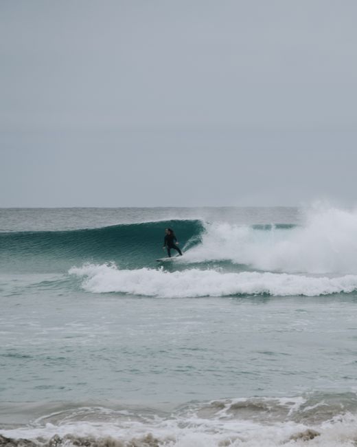 Unrecognizable person in wetsuit riding wave on surfboard in powerful foamy ocean against overcast sky
