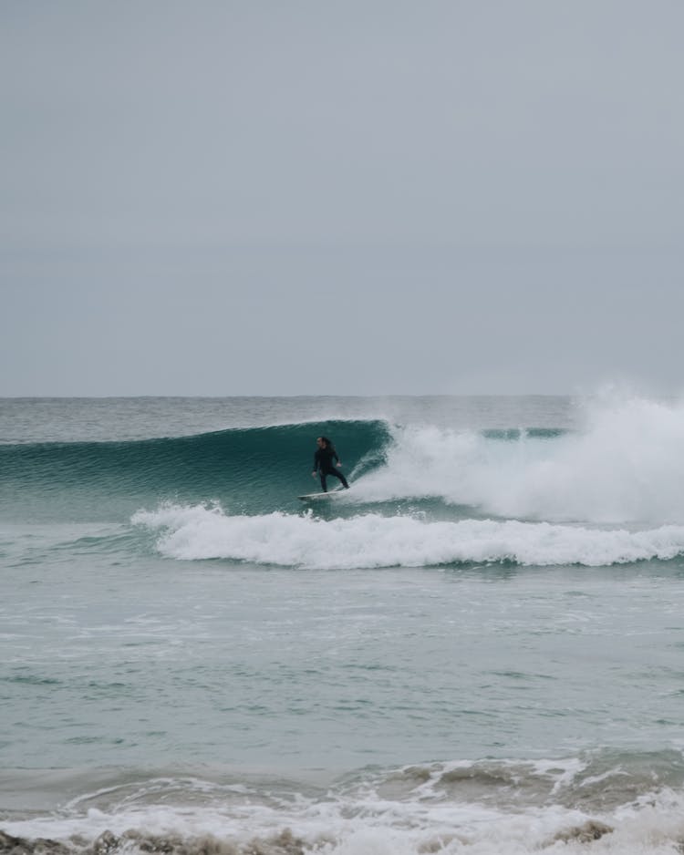 Anonymous Surfer Riding Wave In Foamy Sea Against Cloudy Sky