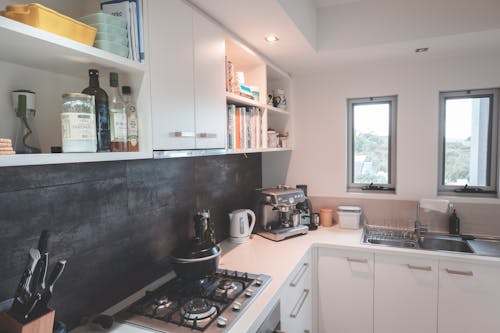 Interior of modern kitchen with white furniture and various appliances and kitchenware in light apartment