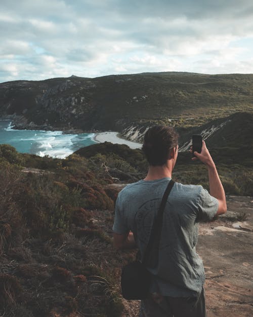 Free Anonymous hiker photographing sea and mountains against cloudy sky Stock Photo