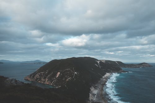 Breathtaking scenery of dramatic cloudy sky over Bald Head walking track and Isthmus Hill surrounded by foamy stormy ocean with sandy beach