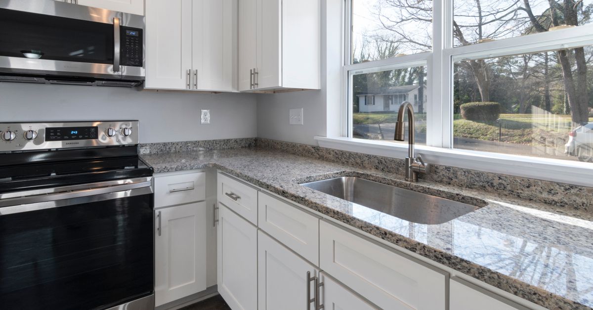 Bright kitchen showcasing granite countertops, stainless steel appliances, and large windows.