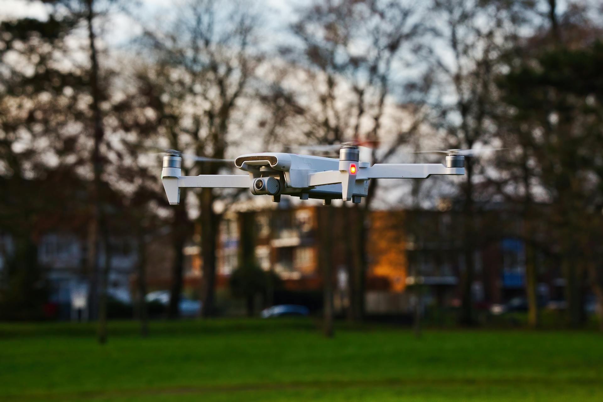 A white drone in flight over a city park during daytime, showcasing modern technology.