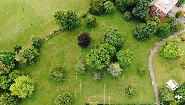 Aerial view of a green park with trees, pathways, and sports markings on grass.