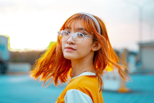 Free Captivating portrait of a young Asian woman with orange hair and glasses, exuding a vibrant and trendy vibe. Stock Photo