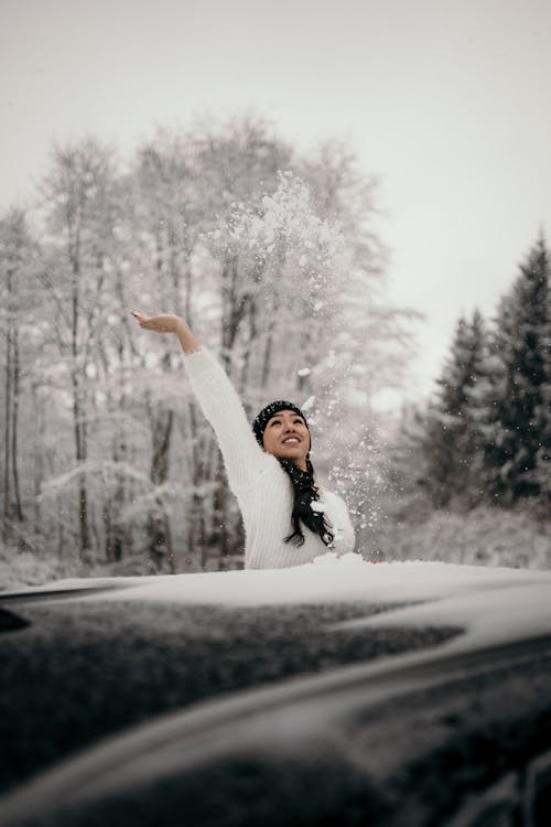 Carefree ethnic female throwing up snow near car