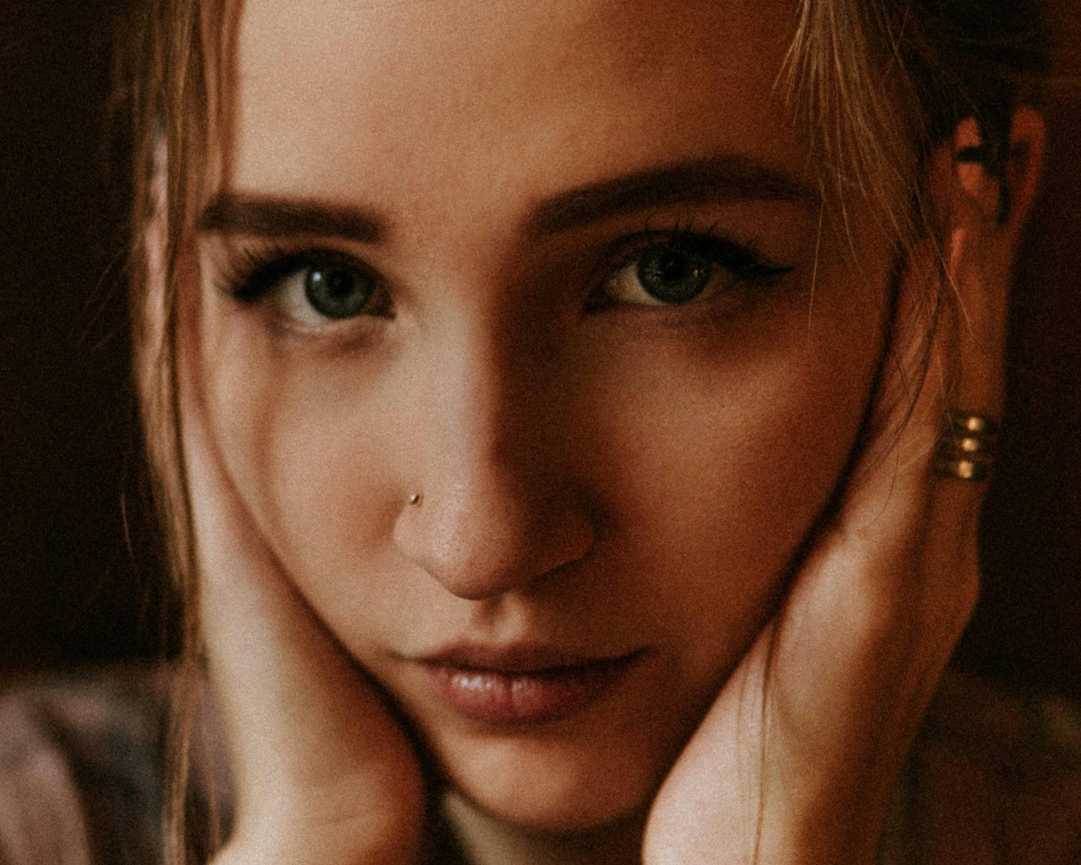 Crop female with eyelashes and piecing on nose touching face gently and looking at camera