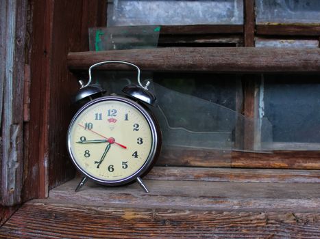 Classic analogue alarm clock on a worn wooden windowsill, evoking nostalgia.