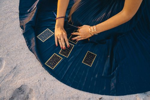 Free A woman elegantly arranges tarot cards on a beach, evoking a sense of mysticism. Stock Photo