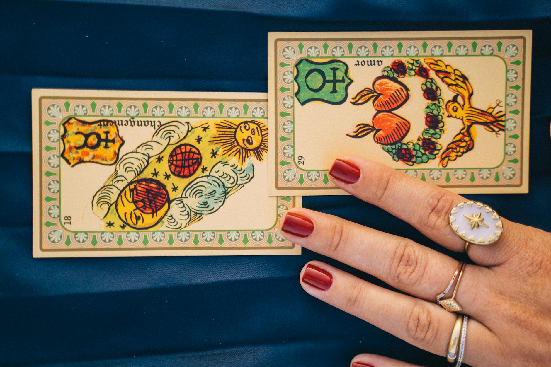 Close-up of tarot cards and hand with rings, set on blue fabric, invoking spiritual and mystical themes.