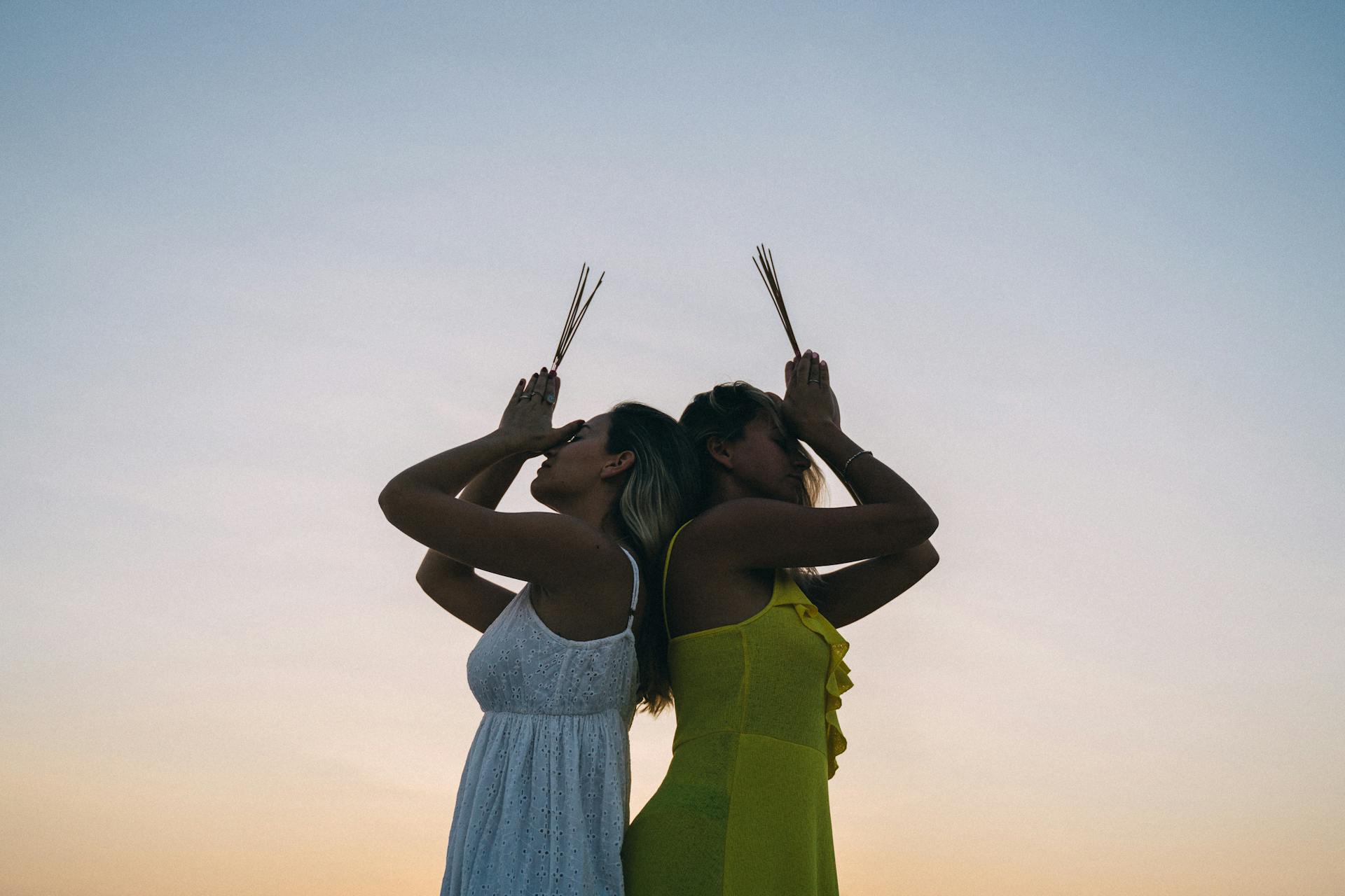 Two women engage in spiritual meditation with incense at sunset, creating a peaceful ambiance.