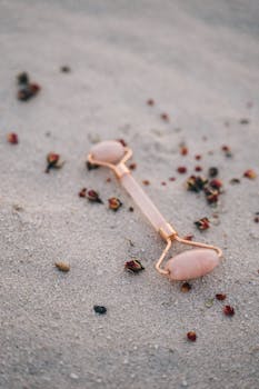 Rose quartz facial roller surrounded by dried flowers on sand, evoking calm and mindfulness.