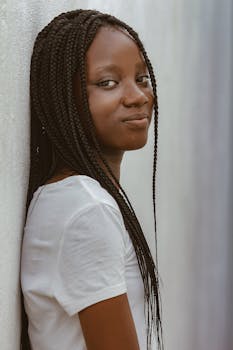 Portrait of a confident woman with long braids against a light background, showcasing modern fashion.
