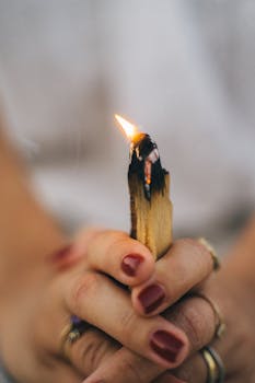 Close-up of a woman holding a lit Palo Santo stick, symbolizing spiritual healing and mindfulness.