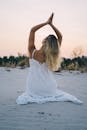 日落时分，身穿白色连衣裙的女子在宁静的海滩上冥想，增强平静和正念