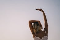 晴朗的天空下，一名妇女在户外举起手臂的背影