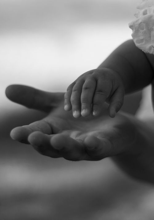 Free A touching black-and-white image of a baby reaching out to an adult's hand, symbolizing care and connection. Stock Photo