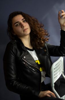A confident brunette woman in a leather jacket posing indoors against a dark background.