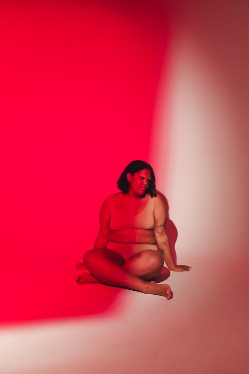 Free Striking studio shot of a plus-size woman seated under dynamic red lighting, embracing body positivity. Stock Photo