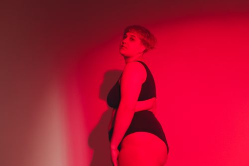 Free Side view of a plus size woman posing confidently in a red studio setting. Stock Photo