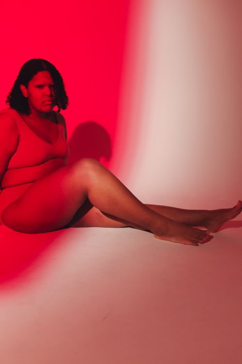 Free Studio shot of a plus-size woman sitting confidently under striking red lighting. Stock Photo