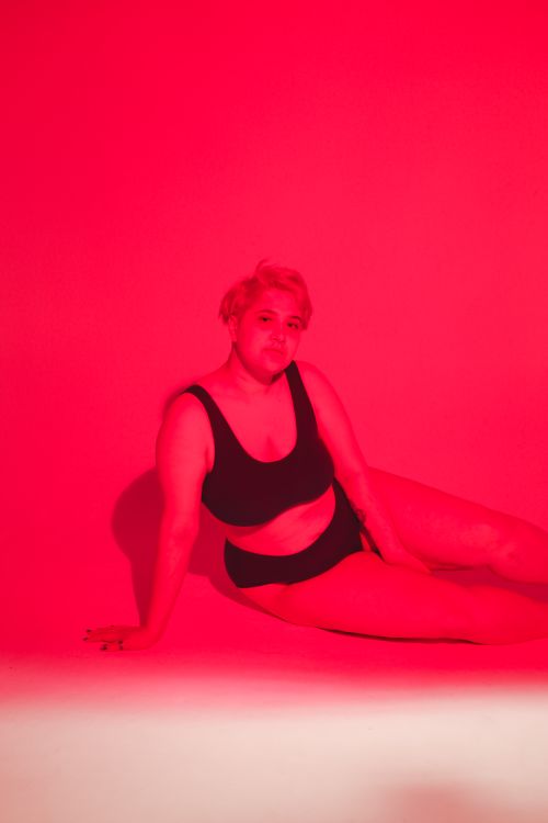 Free Confident plus size woman poses in a red-lit studio, embracing body positivity. Stock Photo