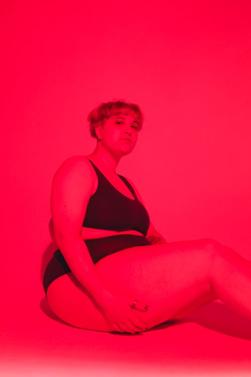 Free A confident plus-size woman posing in a red-hued studio, embracing body positivity. Stock Photo